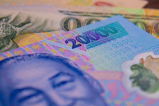 A tight close-up of Vietnamese Dong banknotes, featuring the blue 20,000 bill with Ho Chi Minh's portrait in the foreground and a green 100,000 bill behind it. The focus is on the intricate microprint