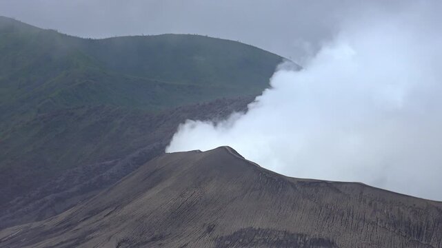 Clouds of smoke coming from crater of Mount Bromo and drifting by, Tengger Semeru national park, East Java, Indonesia. Landscape with erupting volcano in sunny day. Eruption and volcanic activity.