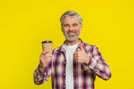 Mature man holds lightweight paper plastic cup, smelling coffee aroma with satisfaction calm expression. Middle-aged guy on yellow background drinking morning coffee, reflecting early routine pleasure - Powered by Adobe