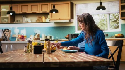 Mature couple serving breakfast together with pastry and warm coffee, bright home kitchen table. Chatting and bonding within a calm morning routine and cozy retirement lifestyle. Camera A.