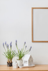 Beautiful Muscari flowers with reed diffuser and house on shelf in light room