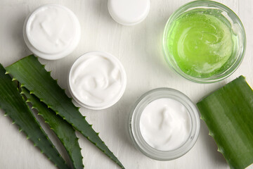 Jars of cosmetic cream and glass bowl of gel with aloe vera leaves on white wooden background