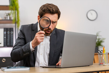 Middle-aged businessman at home office checks laptop screen with magnifier glass finds tiny font error. Freelancer guy at table verifies numbers notes issue and confirms audit result with relief ok.