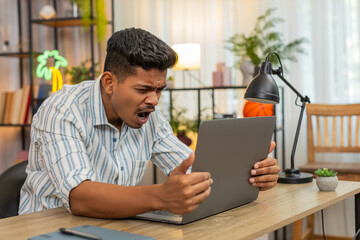 Indian man at home reads laptop update about project loss and sighs feels sad upset by failure. Arabian guy at table checks report sees bad news looks down rubs face and plans fix and retry next step.