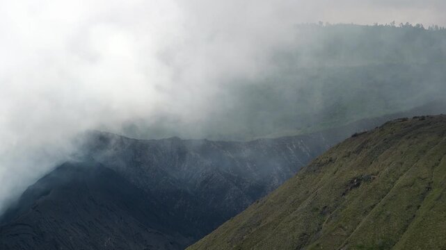 Clouds of smoke coming from crater of Mount Bromo and drifting by, Tengger Semeru national park, East Java, Indonesia. Landscape with erupting volcano in sunny day. Eruption and volcanic activity.