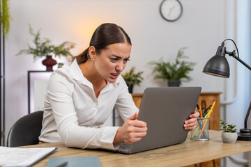 Young businesswoman at home office stares at frozen laptop presses keys and waits tense with sigh....