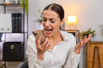 Young businesswoman at home office talks on smartphone argues and waves palm no no with raised voice. Freelancer girl at table disagreement asks for solution sets boundary ends call breathes out firm.