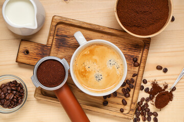 Cup of coffee with powder, beans, portafilter and jug of milk on light wooden background