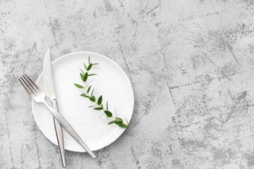 Stylish table setting with plate, cutlery and plant branch on grey grunge background