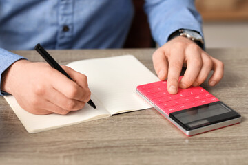 Man writing down something and using calculator at table in office. Closeup