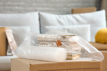 Keys from new house with roll of bubble wrap and books on table in living room at moving day