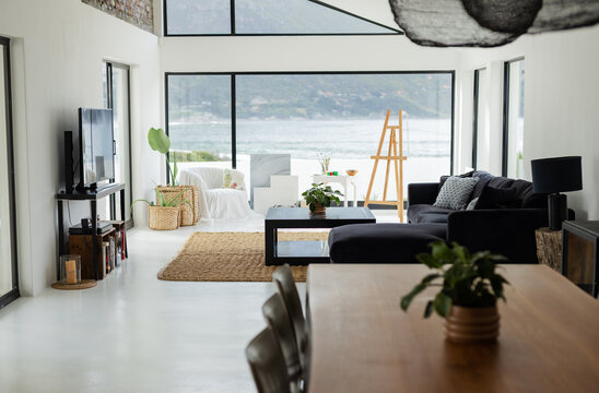 Open-plan living room featuring charcoal sofa, black coffee table on rug, revealing waterfront view