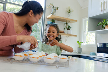 African American mother and daughter decorating cupcakes with piping bag on countertop in kitchen