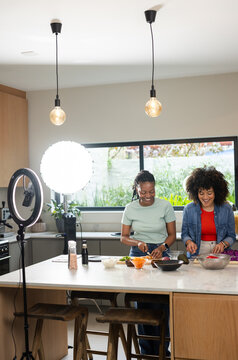 Diverse female friends chopping vegetables at home kitchen island with ring light and LED softbox