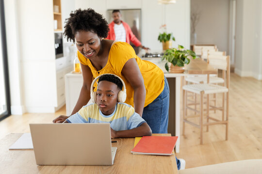 African American family supervising boy studying on laptop with headphones at dining table