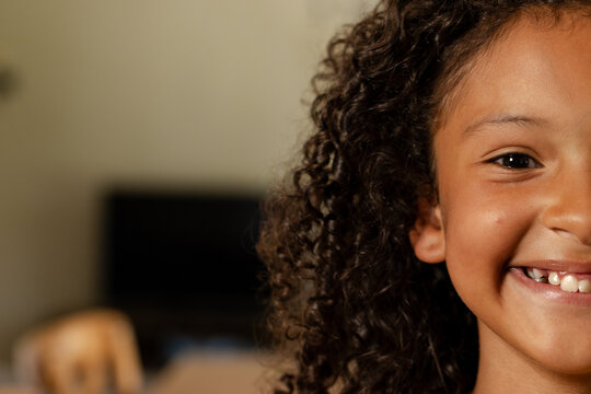 African American child girl smiling with curly hair near wooden chair monitor in home, copy space