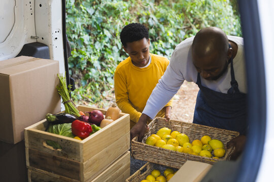 Loading vegetable crates and wicker lemon baskets by African American father and son at cargo van