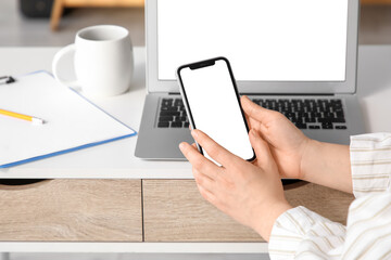 Young woman with blank mobile phone at table in office, closeup