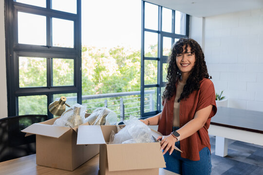 African American woman leaning on cardboard box at wood desk with bubble wrap and brass lamp