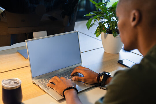 Silver laptop resting beside coffee tumbler on light wood desk in modern office, with potted plant - Powered by Adobe