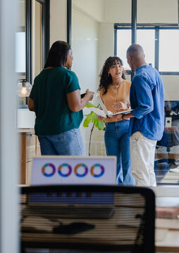 African American coworkers discussing plan while holding open laptop and phone in office bay