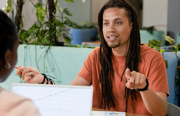 African American coworkers talking on rising line chart on laptop at office man wearing orange tee