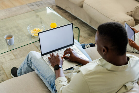 Silver laptop sitting on light sofa near glass coffee table with chips, orange juice, mug, tablet