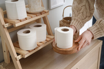 Woman taking roll of toilet paper from wooden cabinet in stylish restroom