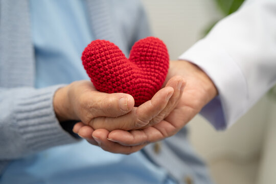 Doctor giving a red heart to senior patient in hospital.