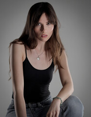 Fototapeta premium Studio portrait of a beautiful brunette woman wearing a black tank top and jeans against a gray background. This image is suitable for fashion beauty and lifestyle projects.