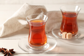 Glasses of Turkish tea with anise stars and sugar cubes on white wooden background