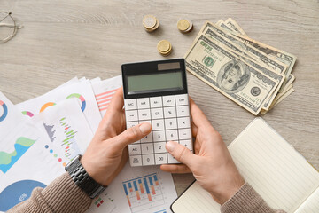 Male hands with calculator counting money at table in office. Top view