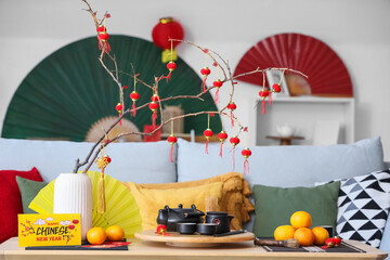 Vase with tree branches, mandarins, tea and card for Chinese New Year celebration on table in living room