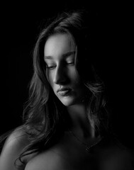 Naklejka premium Monochrome studio portrait of a young woman with long hair on a black background. This image is suitable for fashion beauty and artistic projects.