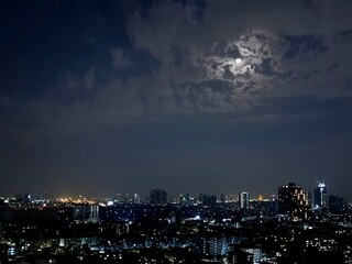 Obraz premium Night Cityscape with Moon Behind Clouds Over Urban Skyline