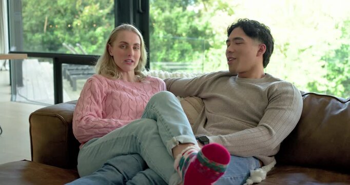 Diverse couple conversing, leaning, nodding, turning toward camera and smiling on sofa at home