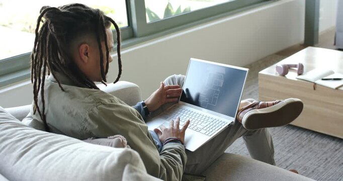 Individual opening silver laptop on couch by window and reviewing floor plan for design