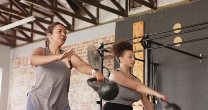 Diverse female workout partners swinging kettlebells in gym focusing on technique and form