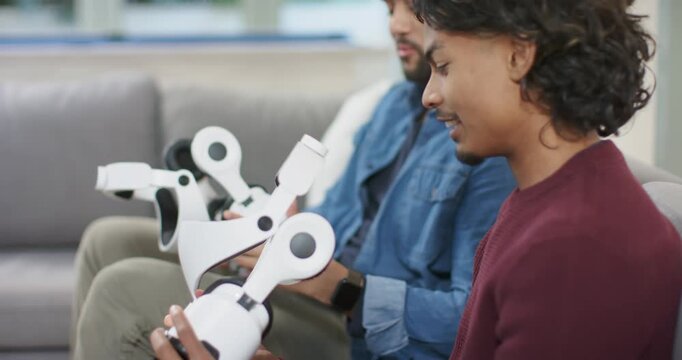 Diverse colleagues gripping robotic exoskeleton segment rotating joints testing range on gray sofa