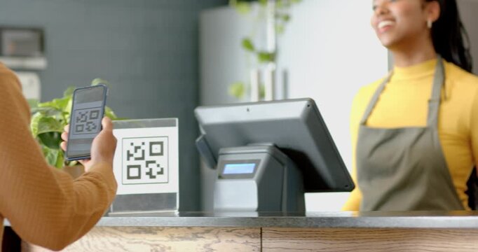Man scanning phone and QR code sign at counter paying while female cashier confirming touchscreen