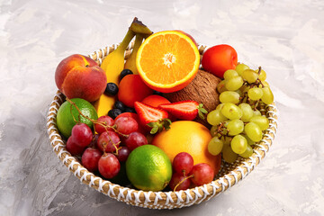 Wicker bowl with different fresh fruits on grey background