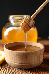 Pouring of sweet honey from dipper into bowl on table
