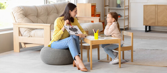 Female psychologist showing picture to little girl at table in office