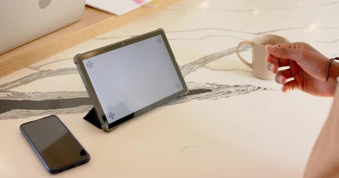 Coffee mug entering frame as woman's hand positioning it on tablet screen over desk for demo