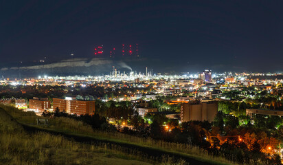 A night view of Billings, Montana. The oil refinery is brightly lit below the Rimrocks cliffs, which are topped with tall red antenna towers