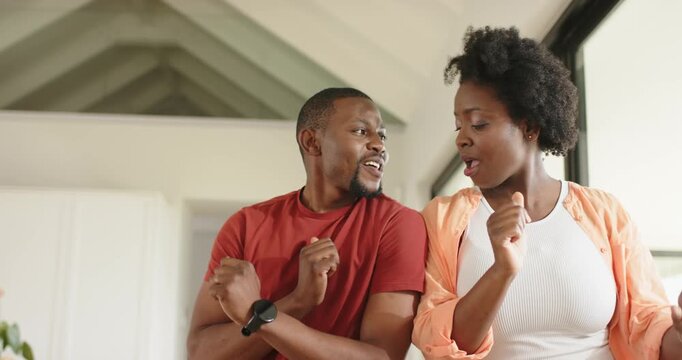 African American couple dancing bending elbows laughing to unseen music in home by large window