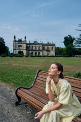 Naklejka premium Woman on bench in park with historic mansion background, relaxation in sunlight, authenticity inclusivity