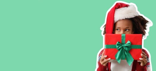 Teenage African-American girl in Santa hat and with Christmas gift on green background with space for text