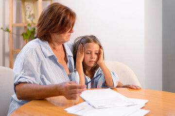Little girl feel unmotivated to do prepare homework with grandmother at table. Caring grandparent studying with small girl child at home, education, school problem concept
