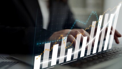 Business professional focused on financial data analysis using a laptop with digital graphs showing growth trends in a modern office space. Copula